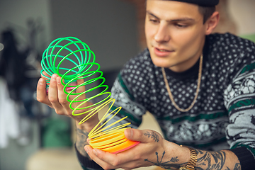 Image showing Portrait of millenial boy using retro toys, meeting things from the past and having fun, exploring rainbow spring toy