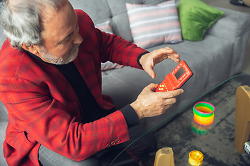 Image showing Portrait of senior man with retro toys, meeting things from the past and having fun, exploring the lifestyle of the nineties, playing with rainbow spring toy and tetris