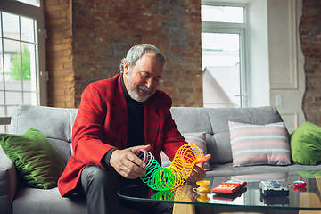 Image showing Portrait of senior man with retro toys, meeting things from the past and having fun, exploring the lifestyle of the nineties, playing with rainbow spring toy