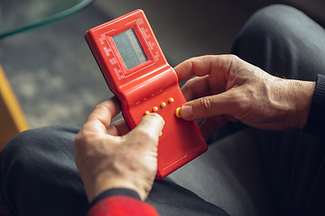 Image showing Close up of senior man with retro toys, meeting things from the past and having fun, exploring the lifestyle of the nineties, playing with tetris