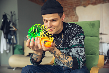 Image showing Portrait of millenial boy using retro toys, meeting things from the past and having fun, exploring rainbow spring toy