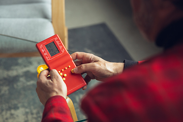 Image showing Close up of senior man with retro toys, meeting things from the past and having fun, exploring the lifestyle of the nineties, playing with tetris