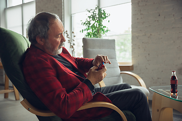 Image showing Portrait of senior man with retro toys, meeting things from the past and having fun, exploring the lifestyle of the nineties, playing with tamagotchi