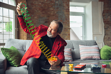 Image showing Portrait of senior man with retro toys, meeting things from the past and having fun, exploring the lifestyle of the nineties, playing with rainbow spring toy