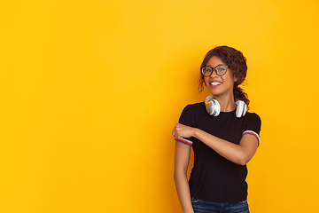 Image showing African-american beautiful young woman\'s portrait with wireless headphones on yellow studio background, emotional and expressive. Copyspace for ad.