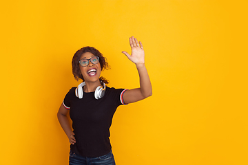 Image showing African-american beautiful young woman\'s portrait with wireless headphones on yellow studio background, emotional and expressive. Copyspace for ad.