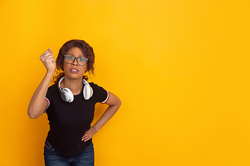 Image showing African-american beautiful young woman\'s portrait with wireless headphones on yellow studio background, emotional and expressive. Copyspace for ad.