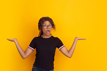 Image showing African-american beautiful young woman\'s portrait on yellow studio background, emotional and expressive. Copyspace for ad.