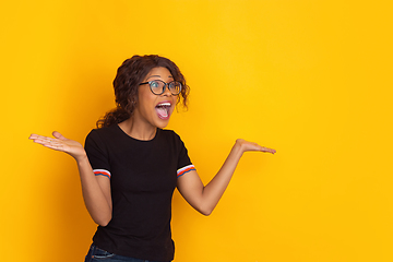 Image showing African-american beautiful young woman\'s portrait on yellow studio background, emotional and expressive. Copyspace for ad.