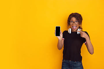 Image showing African-american beautiful young woman\'s portrait with wireless headphones on yellow studio background, emotional and expressive. Copyspace for ad.