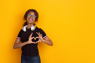 Image showing African-american beautiful young woman\'s portrait with wireless headphones on yellow studio background, emotional and expressive. Copyspace for ad.