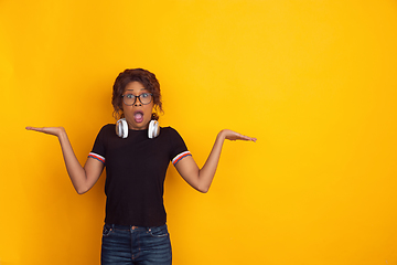 Image showing African-american beautiful young woman\'s portrait with wireless headphones on yellow studio background, emotional and expressive. Copyspace for ad.