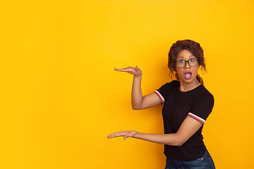 Image showing African-american beautiful young woman\'s portrait on yellow studio background, emotional and expressive. Copyspace for ad.