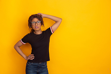 Image showing African-american beautiful young woman\'s portrait on yellow studio background, emotional and expressive. Copyspace for ad.