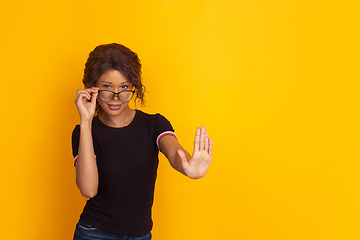 Image showing African-american beautiful young woman\'s portrait on yellow studio background, emotional and expressive. Copyspace for ad.