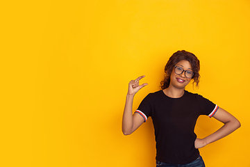 Image showing African-american beautiful young woman\'s portrait on yellow studio background, emotional and expressive. Copyspace for ad.