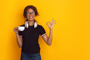 Image showing African-american beautiful young woman\'s portrait with wireless headphones on yellow studio background, emotional and expressive. Copyspace for ad.