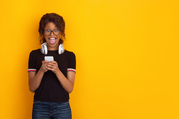 Image showing African-american beautiful young woman\'s portrait with wireless headphones on yellow studio background, emotional and expressive. Copyspace for ad.