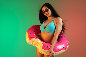 Image showing Fashion portrait of young fit and sportive woman in blue luxury swimwear with rubber donut and stylish sunglasses on gradient background. Perfect body ready for summertime.