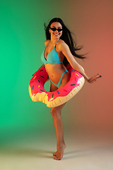 Image showing Fashion portrait of young fit and sportive woman in blue luxury swimwear with rubber donut and stylish sunglasses on gradient background. Perfect body ready for summertime.