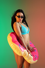 Image showing Fashion portrait of young fit and sportive woman in blue luxury swimwear with rubber donut and stylish sunglasses on gradient background. Perfect body ready for summertime.