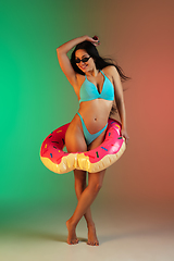 Image showing Fashion portrait of young fit and sportive woman in blue luxury swimwear with rubber donut and stylish sunglasses on gradient background. Perfect body ready for summertime.