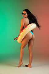 Image showing Fashion portrait of young fit and sportive woman in blue luxury swimwear with rubber donut and stylish sunglasses on gradient background. Perfect body ready for summertime.