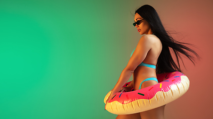 Image showing Fashion portrait of young fit and sportive woman in blue luxury swimwear with rubber donut and stylish sunglasses on gradient background. Perfect body ready for summertime. Flyer.