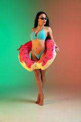 Image showing Fashion portrait of young fit and sportive woman in blue luxury swimwear with rubber donut and stylish sunglasses on gradient background. Perfect body ready for summertime.