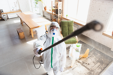 Image showing Coronavirus Pandemic. A disinfector in a protective suit and mask sprays disinfectants in the house or office