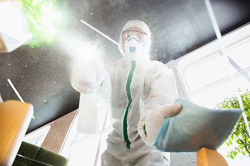 Image showing Coronavirus Pandemic. A disinfector in a protective suit and mask sprays disinfectants in the house or office