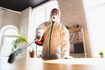 Image showing Coronavirus Pandemic. A disinfector in a protective suit and mask sprays disinfectants in the house or office