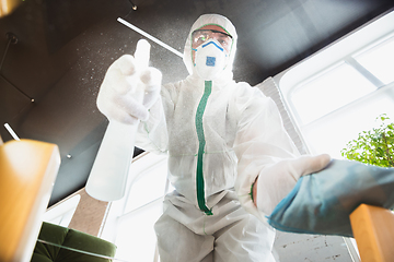 Image showing Coronavirus Pandemic. A disinfector in a protective suit and mask sprays disinfectants in the house or office