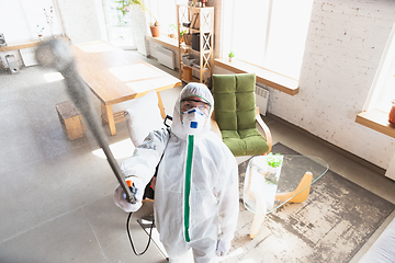 Image showing Coronavirus Pandemic. A disinfector in a protective suit and mask sprays disinfectants in the house or office