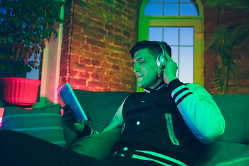 Image showing Cinematic portrait of handsome young man using devices, gadgets in neon lighted interior. Youth culture, bright colors