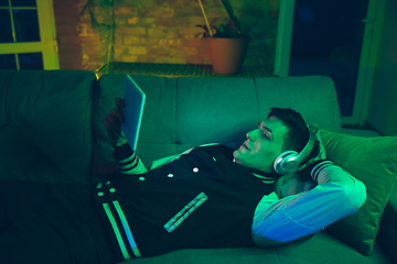 Image showing Cinematic portrait of handsome young man using devices, gadgets in neon lighted interior. Youth culture, bright colors