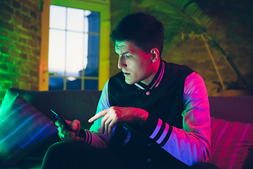 Image showing Cinematic portrait of handsome young man using devices, gadgets in neon lighted interior. Youth culture, bright colors