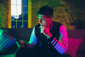 Image showing Cinematic portrait of handsome young man using devices, gadgets in neon lighted interior. Youth culture, bright colors