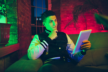 Image showing Cinematic portrait of handsome young man using devices, gadgets in neon lighted interior. Youth culture, bright colors