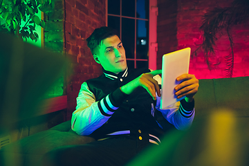 Image showing Cinematic portrait of handsome young man using devices, gadgets in neon lighted interior. Youth culture, bright colors