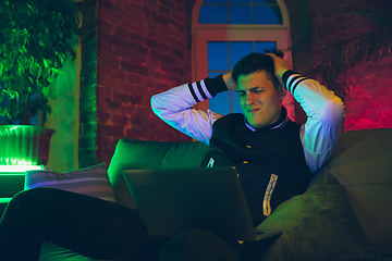 Image showing Cinematic portrait of handsome young man using devices, gadgets in neon lighted interior. Youth culture, bright colors