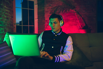 Image showing Cinematic portrait of handsome young man using devices, gadgets in neon lighted interior. Youth culture, bright colors