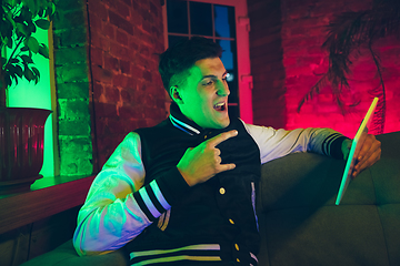 Image showing Cinematic portrait of handsome young man using devices, gadgets in neon lighted interior. Youth culture, bright colors