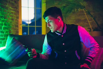 Image showing Cinematic portrait of handsome young man using devices, gadgets in neon lighted interior. Youth culture, bright colors