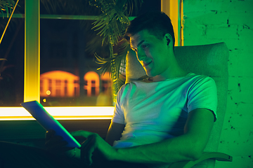 Image showing Cinematic portrait of handsome young man using devices, gadgets in neon lighted interior. Youth culture, bright colors