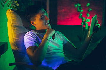 Image showing Cinematic portrait of handsome young man using devices, gadgets in neon lighted interior. Youth culture, bright colors