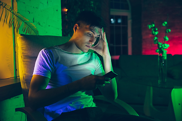 Image showing Cinematic portrait of handsome young man using devices, gadgets in neon lighted interior. Youth culture, bright colors