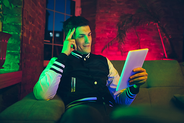 Image showing Cinematic portrait of handsome young man using devices, gadgets in neon lighted interior. Youth culture, bright colors