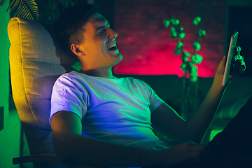 Image showing Cinematic portrait of handsome young man using devices, gadgets in neon lighted interior. Youth culture, bright colors