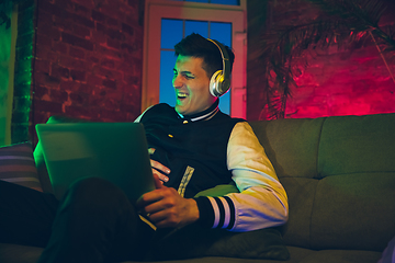 Image showing Cinematic portrait of handsome young man using devices, gadgets in neon lighted interior. Youth culture, bright colors